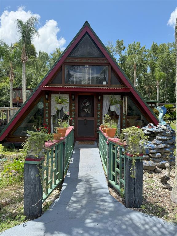 A wooden A-frame house features a front walkway with green railings and potted plants — 3841 ARBOR AVENUE, BUNNELL, FL