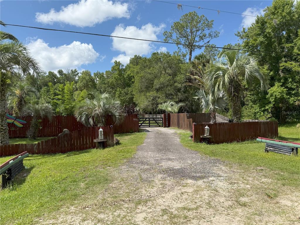 A gravel driveway leads to a gated entrance surrounded by a wooden fence and trees — 3841 ARBOR AVENUE, BUNNELL, FL