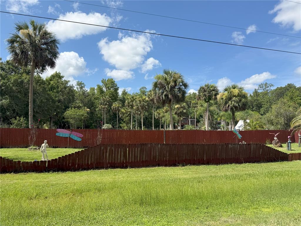 A red wooden fence encloses a grassy backyard with palm trees and decorative lawn ornaments — 3841 ARBOR AVENUE, BUNNELL, FL