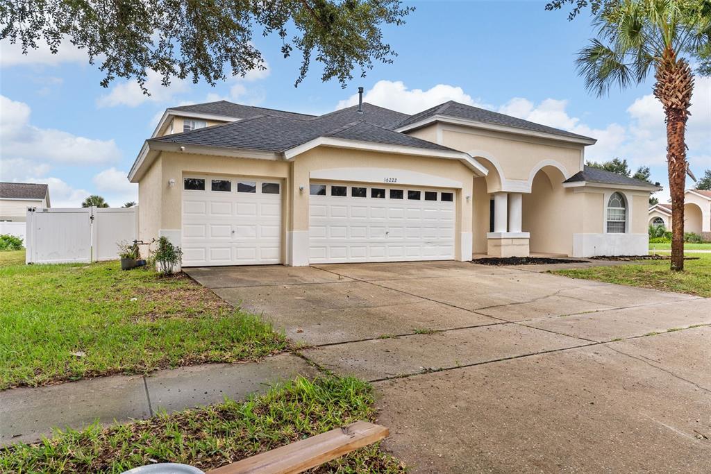A beige single-story house with a three-car garage and a palm tree in the front yard — 16222 EGRET HILL STREET, CLERMONT, FL