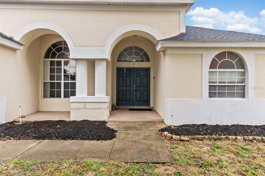 The exterior of a house features a blue double front door, arched windows, and a concrete walkway — 16222 EGRET HILL STREET, CLERMONT, FL