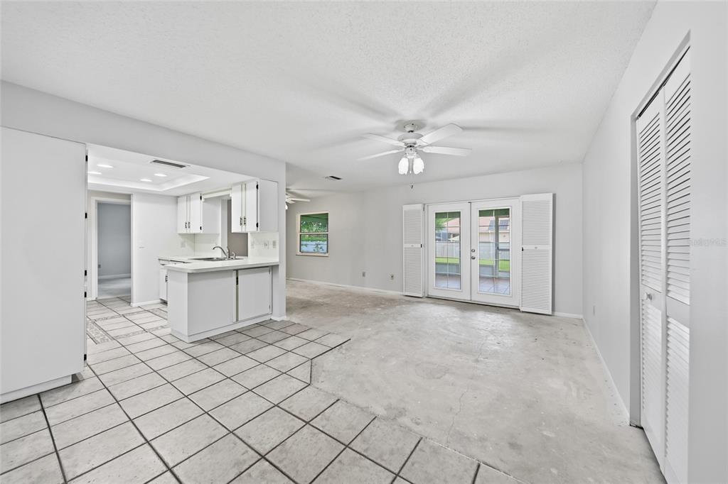 A kitchen with white cabinets and tiled floors opens into a living area with French doors — 5608 4TH AVENUE NW, BRADENTON, FL