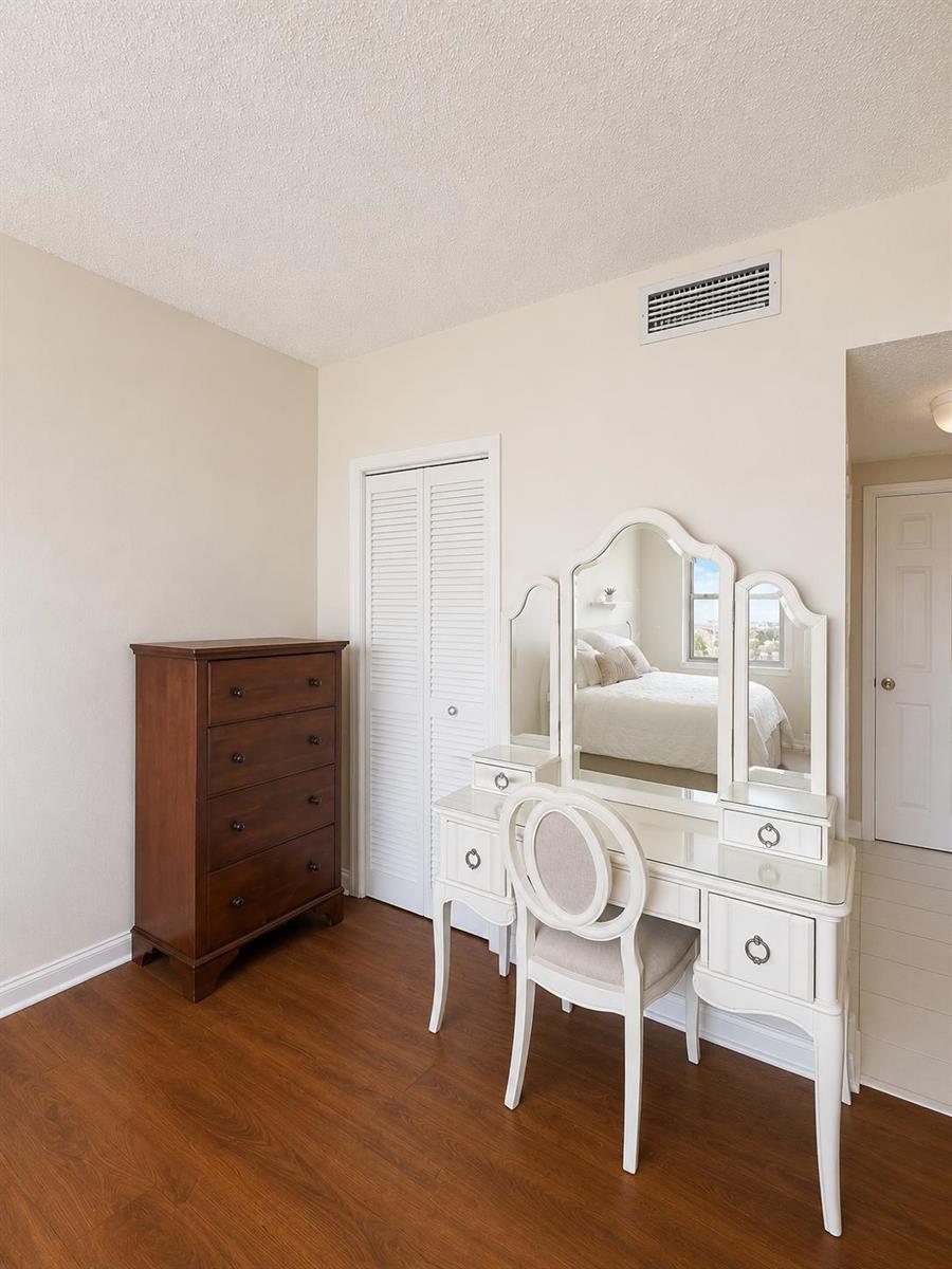 A bedroom features a dark wood dresser, a white vanity set with a mirror, and wood-look flooring — 1985 S Ocean Drive # 22n, FL 33009, FL