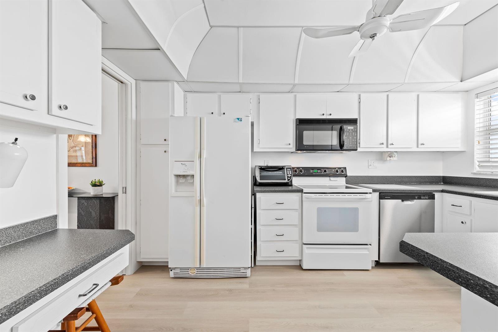 A white kitchen features a refrigerator, stove, microwave, dishwasher, and dark gray countertops — 3300 S Ocean Boulevard # c, Highland Beach FL 33487, HIGHLAND BEACH, FL