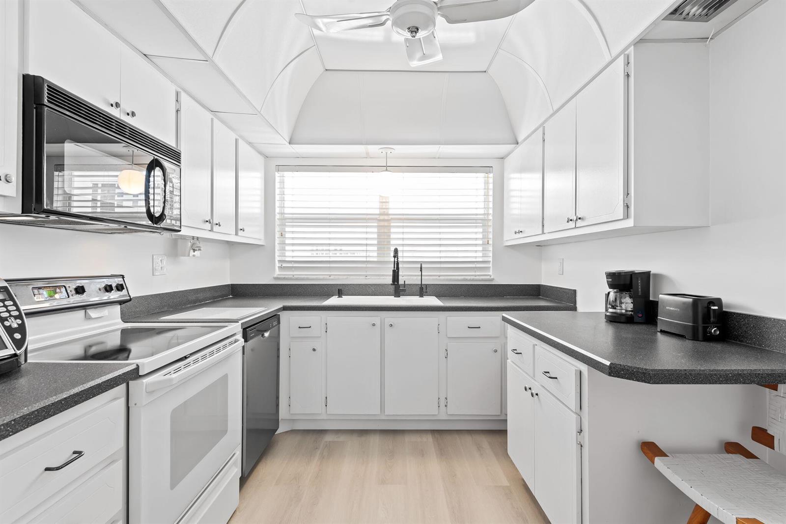 A galley kitchen features white cabinets, dark countertops, a white stove, and a window — 3300 S Ocean Boulevard # c, Highland Beach FL 33487, HIGHLAND BEACH, FL