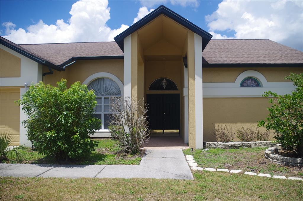 A tan stucco house with a covered entryway, arched windows, and a dark shingled roof — 4207 ELBA PLACE, VALRICO, FL