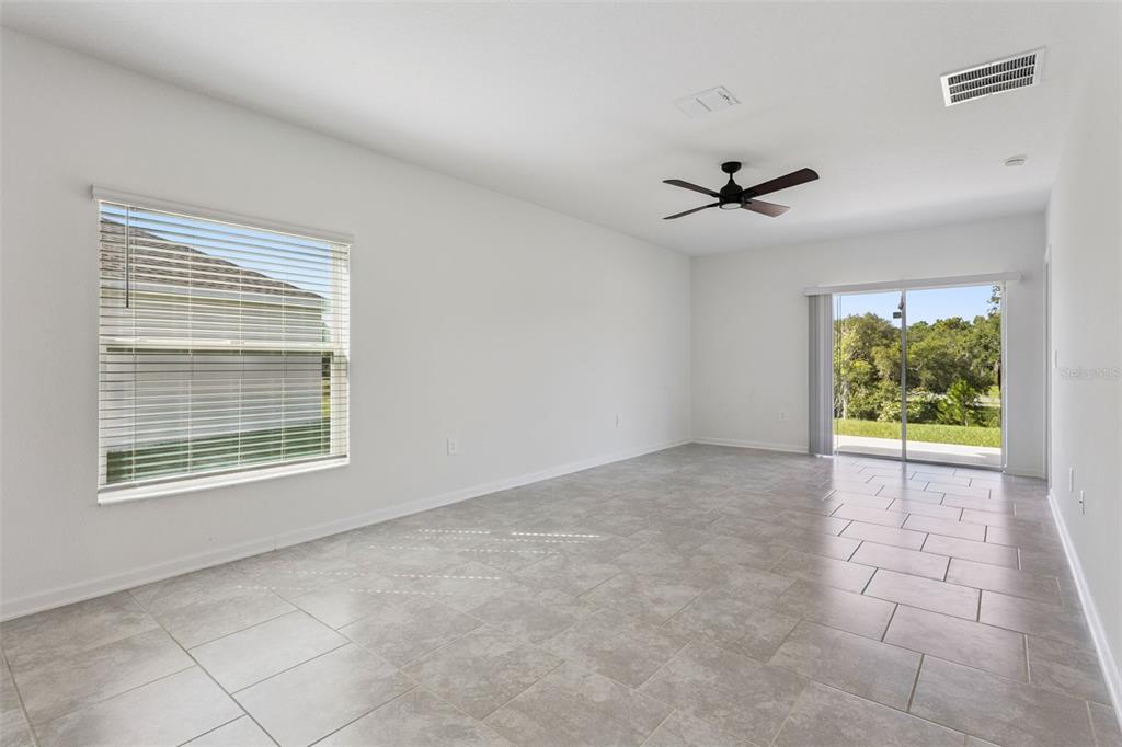 An empty room with white walls, gray tile flooring, a ceiling fan, and sliding glass doors — 26180 FEATHERGRASS CIRCLE, LEESBURG, FL