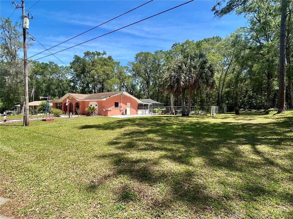 A peach-colored, single-story house sits on a large, grassy lot surrounded by trees — 4047 S GARLAND TERRACE, INVERNESS, FL