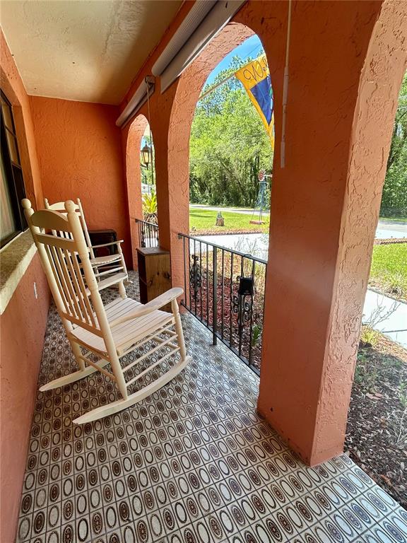 A covered porch features two wooden rocking chairs, patterned tile flooring, and arched stucco openings — 4047 S GARLAND TERRACE, INVERNESS, FL