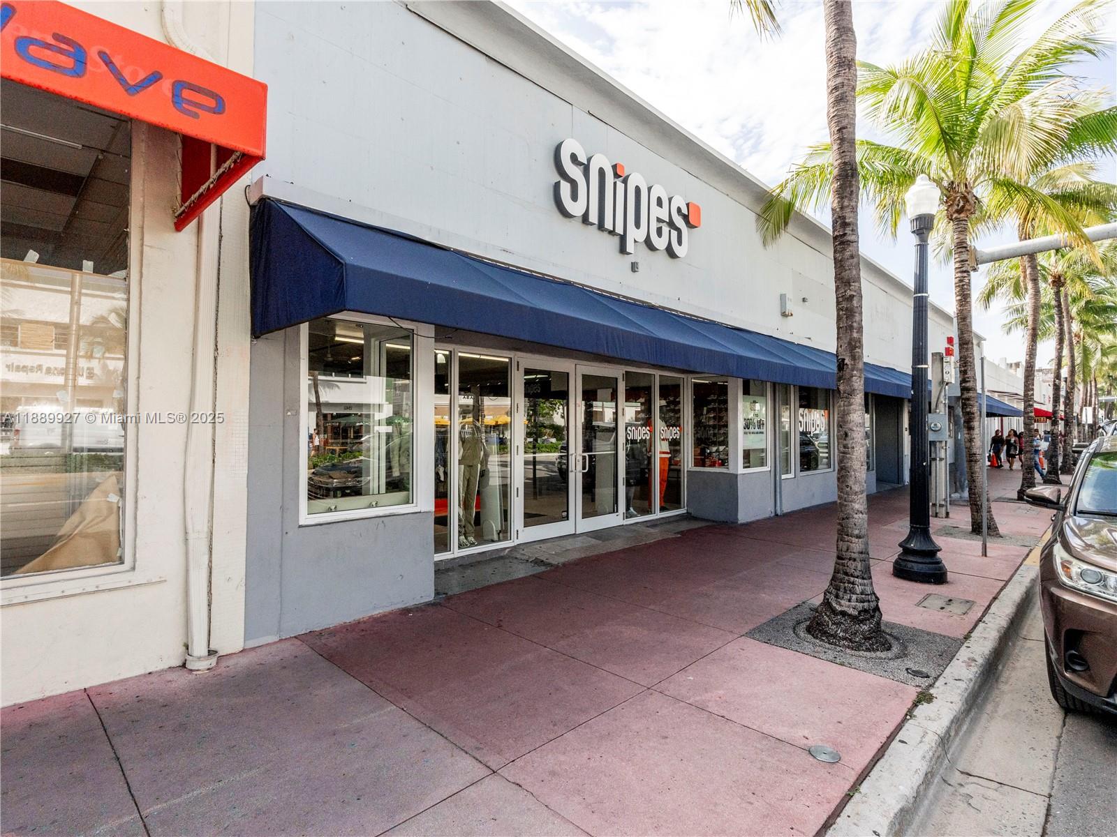 A Snipes retail store exterior features a blue awning, glass doors, and palm trees — 1345 Washington Ave, Miami Beach FL 33139, MIAMI BEACH, FL