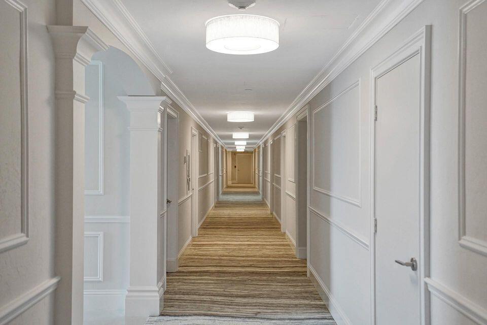 A long hotel hallway features white paneled walls, striped carpeting, and multiple drum ceiling lights — 701 E Camino Real # 4b, Boca Raton FL 33432, BOCA RATON, FL
