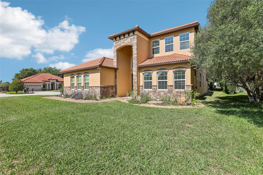 A two-story stucco house with a stone facade, tile roof, and a large front lawn — 10151 YONAOMI CIRCLE, CLERMONT, FL