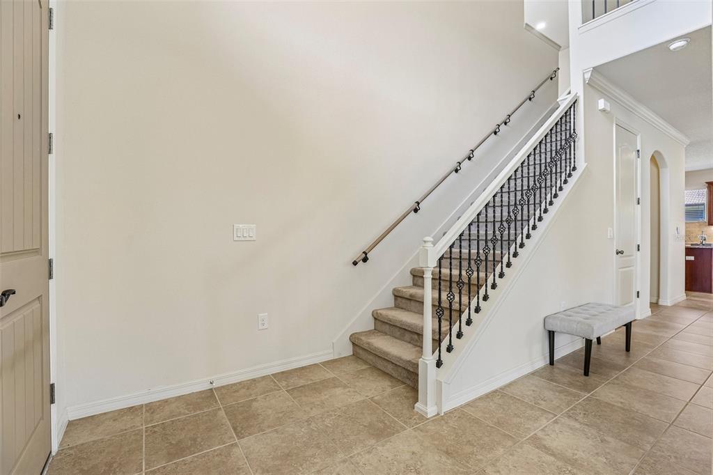 An entryway features beige tile flooring, a carpeted staircase with iron railings, and a bench — 10151 YONAOMI CIRCLE, CLERMONT, FL