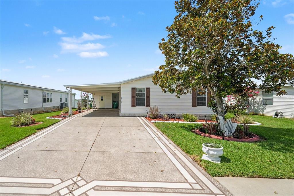 A single-story manufactured home with a concrete driveway, carport, and a large tree in front — 37536 GILL AVENUE, ZEPHYRHILLS, FL
