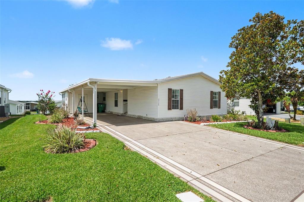 A single-story manufactured home with a concrete driveway, attached carport, and a large magnolia tree — 37536 GILL AVENUE, ZEPHYRHILLS, FL