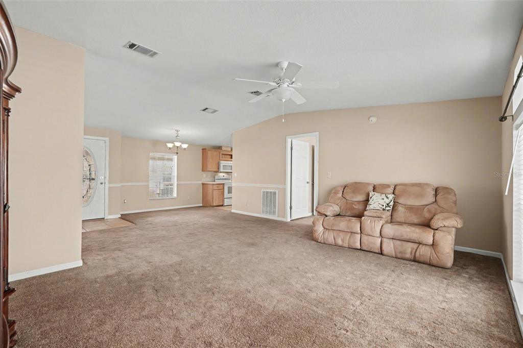 A living room with beige walls, brown carpeting, a ceiling fan, and an adjacent kitchen — 37536 GILL AVENUE, ZEPHYRHILLS, FL