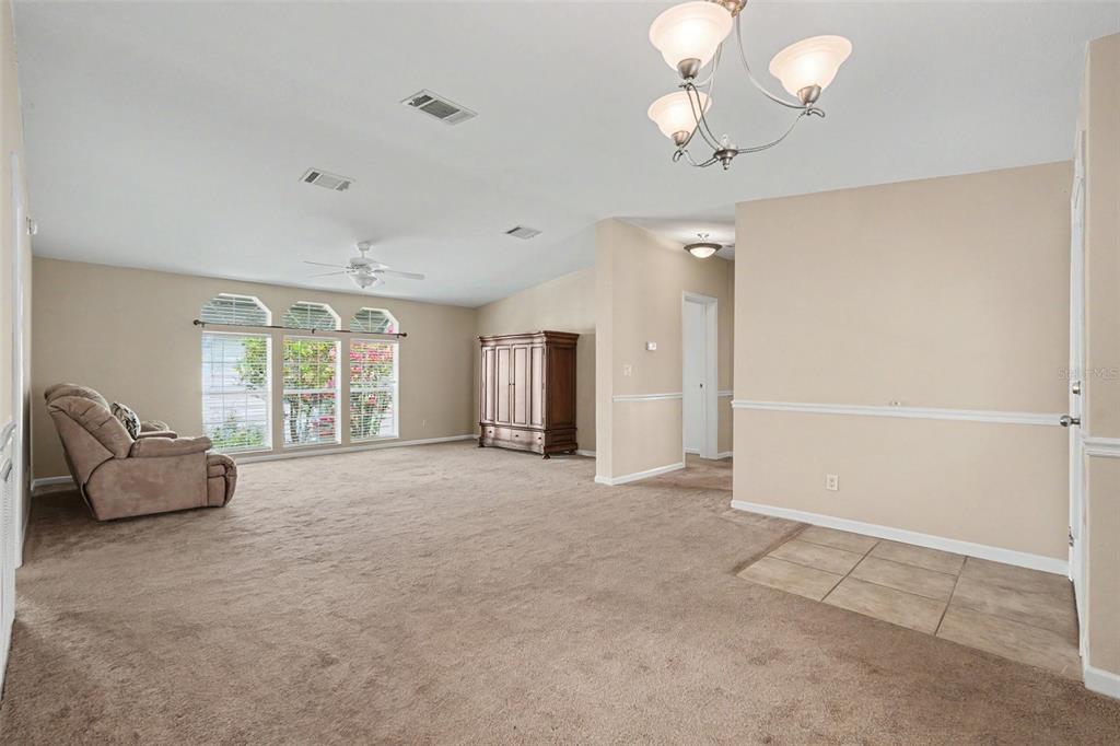 A spacious living room features beige carpeting, a ceiling fan, and a large wooden armoire — 37536 GILL AVENUE, ZEPHYRHILLS, FL