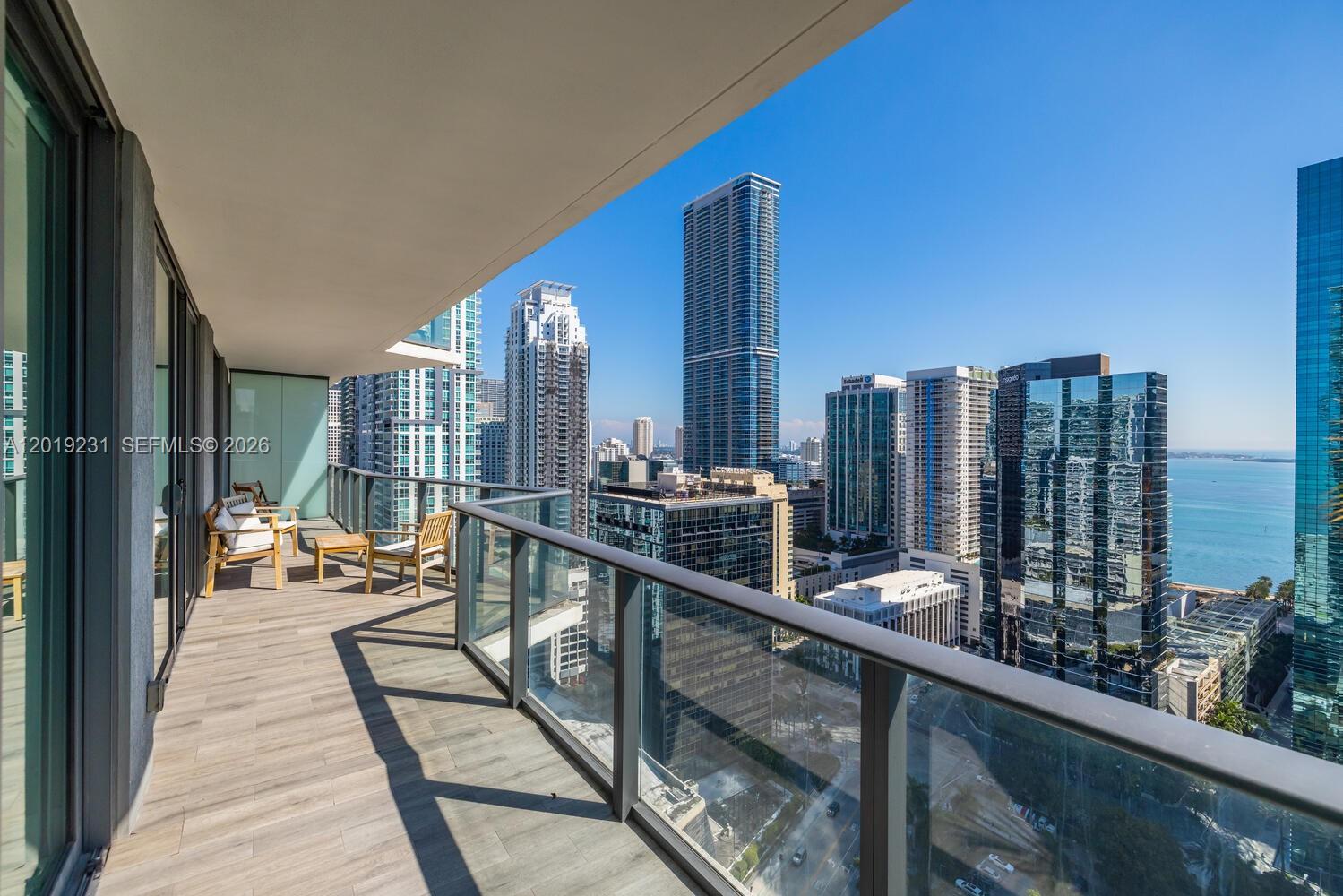 A high-rise balcony features wood-look flooring, glass railings, and a view of city skyscrapers — 1300 S Miami Ave # 2602, Miami FL 33130, MIAMI, FL