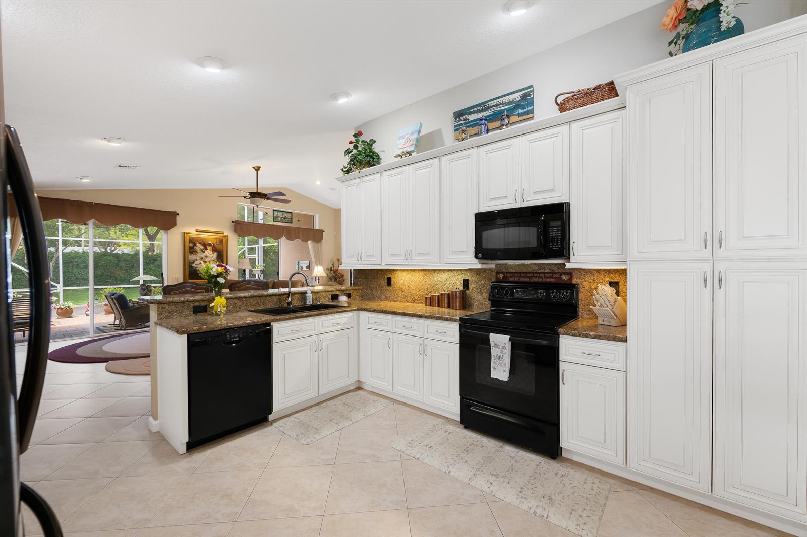 A kitchen with white cabinets, black appliances, and granite countertops opens to a living area — 5185 Glenville Drive, Boynton Beach FL 33437, BOYNTON BEACH, FL