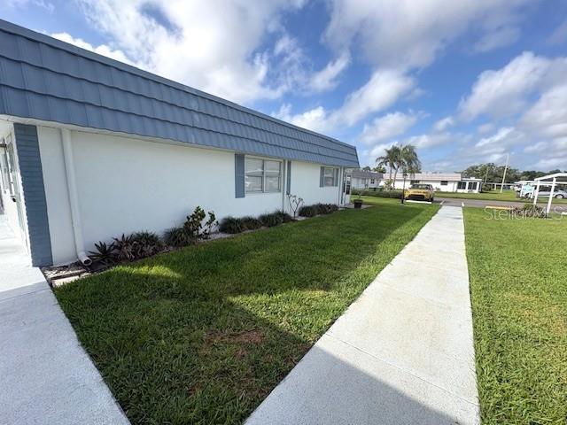 A white building with a blue metal roof sits beside a concrete sidewalk and lawn — 1901 ANDOVER WAY UNIT 38, SUN CITY CENTER, FL