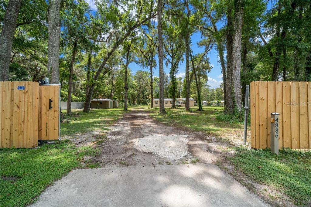 A gravel driveway leads through a wooden gate toward a house surrounded by tall trees — 4886 E HIGHWAY 316, CITRA, FL