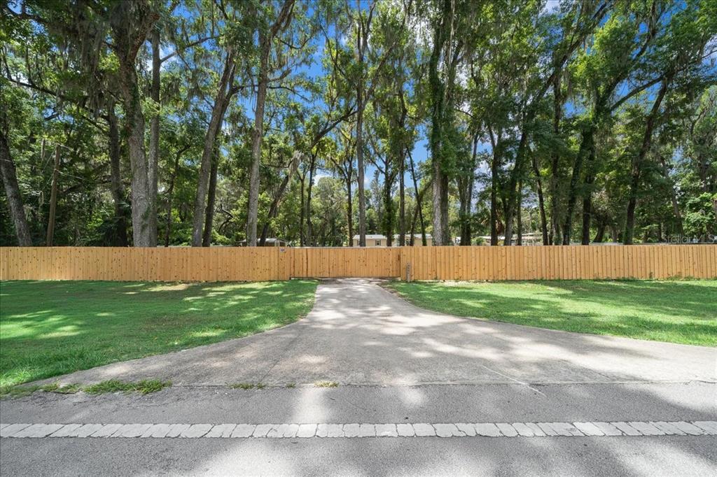 A concrete driveway leads to a wooden fence and gate in front of tall trees — 4886 E HIGHWAY 316, CITRA, FL