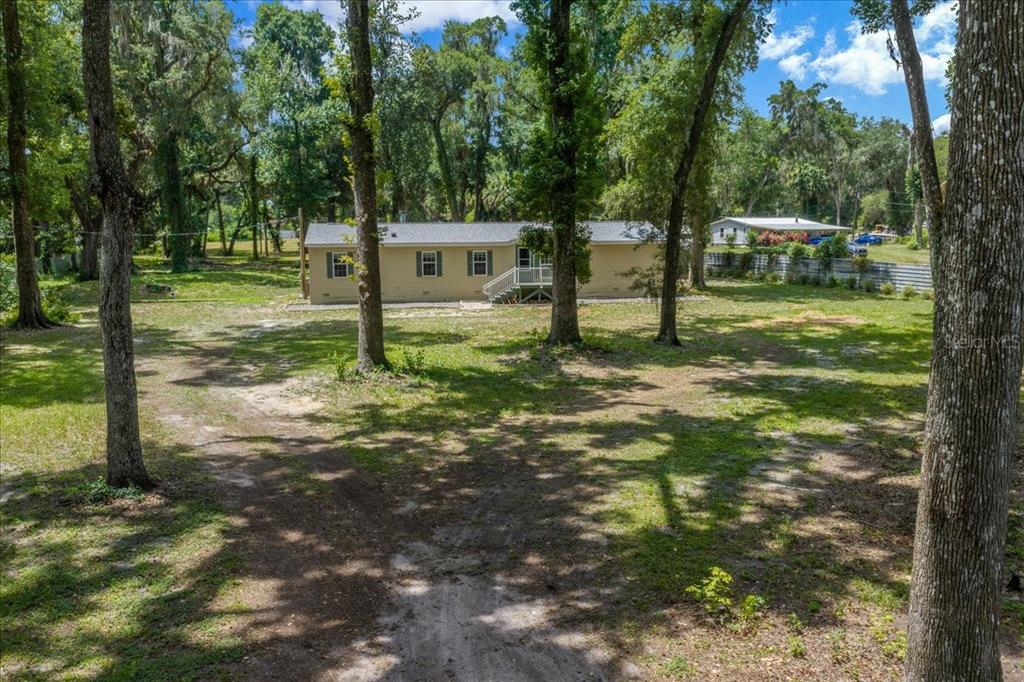 A tan manufactured home sits on a large, grassy lot shaded by numerous mature trees — 4886 E HIGHWAY 316, CITRA, FL