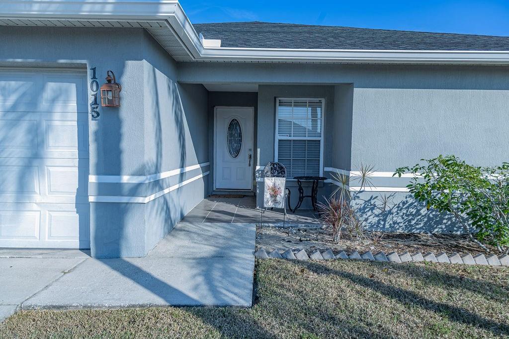 The exterior of a gray house features a white garage door, a front entrance, and landscaping — 1015 HIGHLAND CREST CIRCLE, LAKE WALES, FL