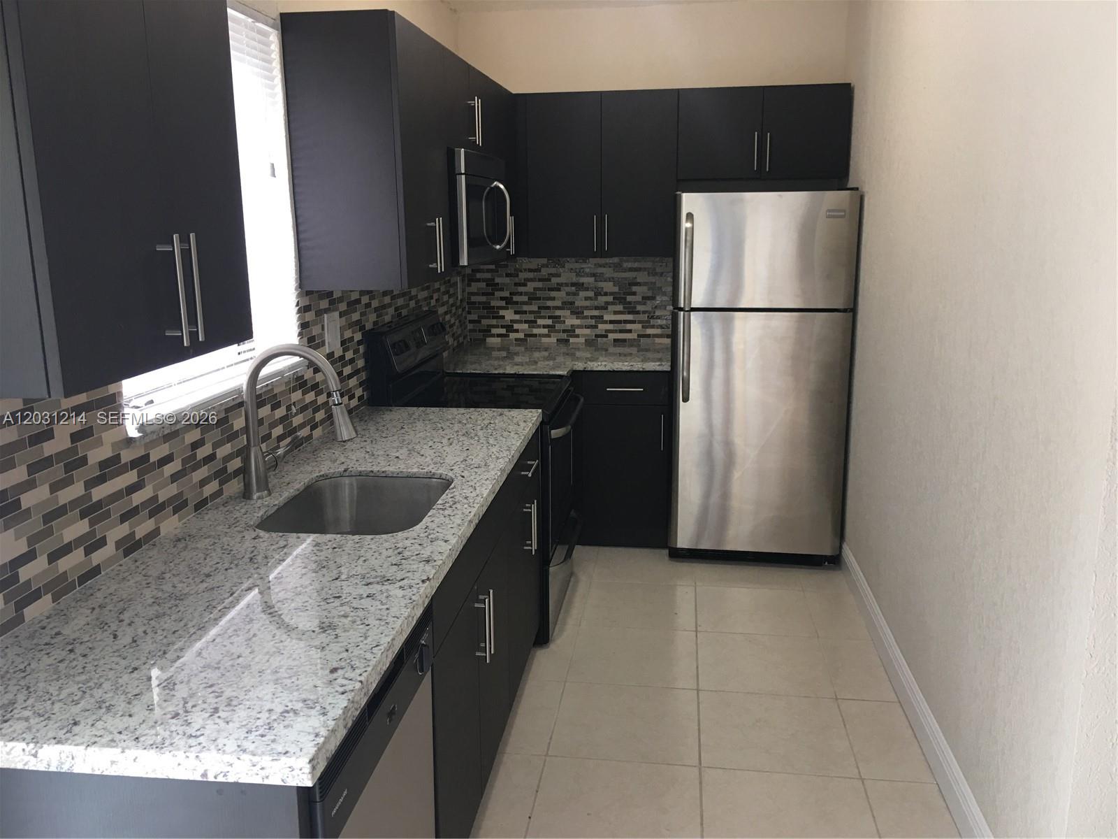 A kitchen features dark cabinets, granite countertops, stainless steel appliances, and a mosaic tile backsplash — 1594 NE 155th Ter, North Miami Beach FL 33162, NORTH MIAMI BEACH, FL