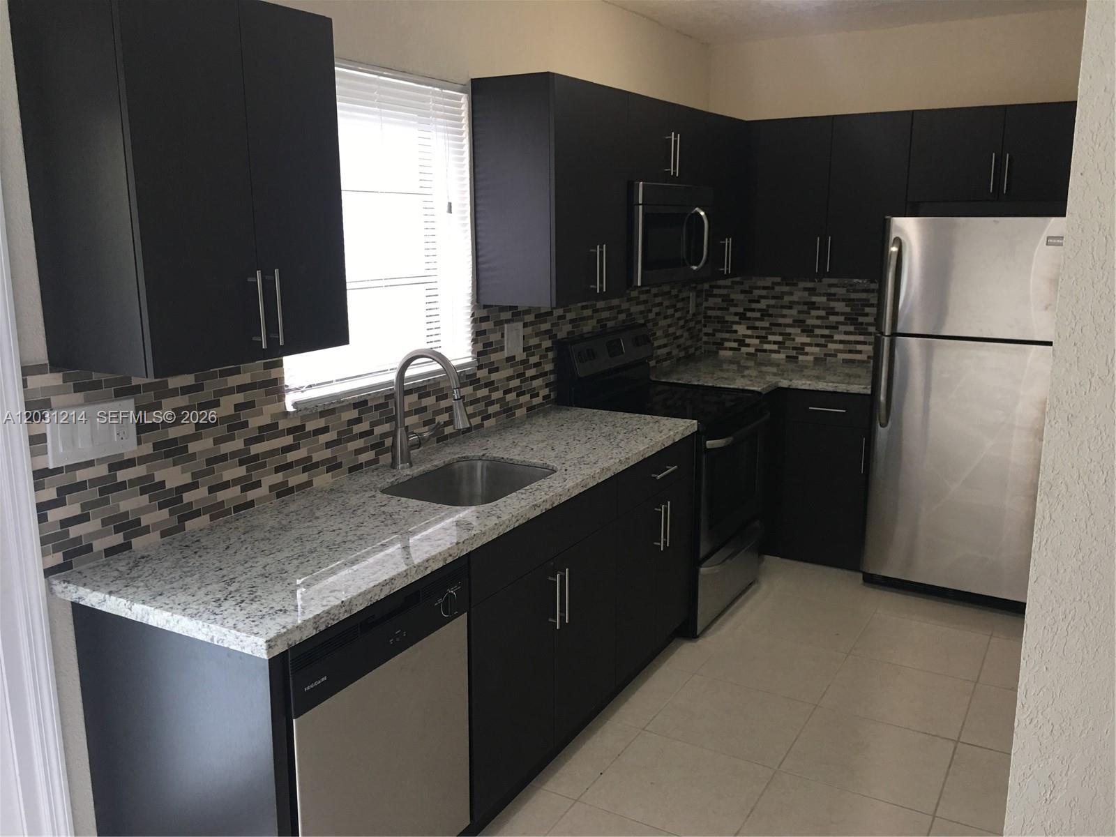 A kitchen features dark cabinets, granite countertops, stainless steel appliances, and a tiled backsplash — 1594 NE 155th Ter, North Miami Beach FL 33162, NORTH MIAMI BEACH, FL
