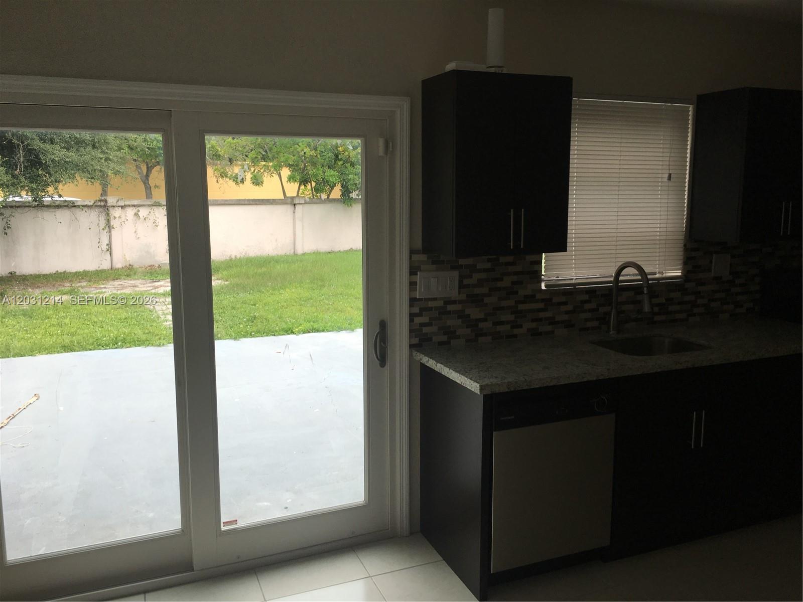 A kitchen with dark cabinets and granite countertops sits next to a sliding glass door — 1594 NE 155th Ter, North Miami Beach FL 33162, NORTH MIAMI BEACH, FL