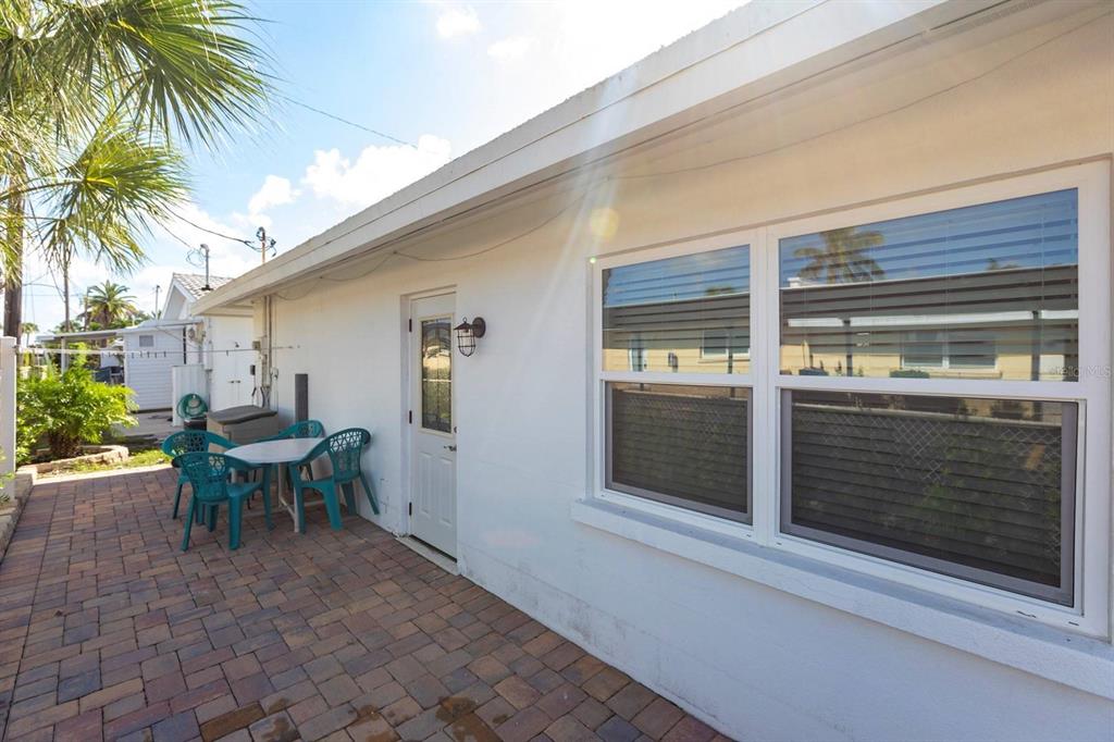 A white exterior wall features a door, a window with blinds, and a brick patio — 6020 MIDNIGHT PASS ROAD UNIT 5, SARASOTA, FL