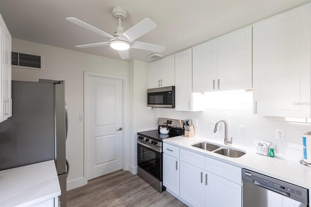 A kitchen with white cabinets, stainless steel appliances, a ceiling fan, and a double sink — 6020 MIDNIGHT PASS ROAD UNIT 5, SARASOTA, FL