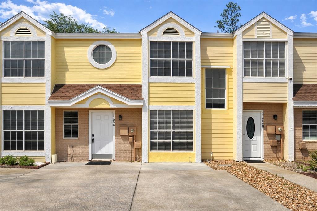 A two-story yellow townhouse exterior with a concrete driveway and two white front doors — 11008 YORKSHIRE RIDGE COURT, ORLANDO, FL