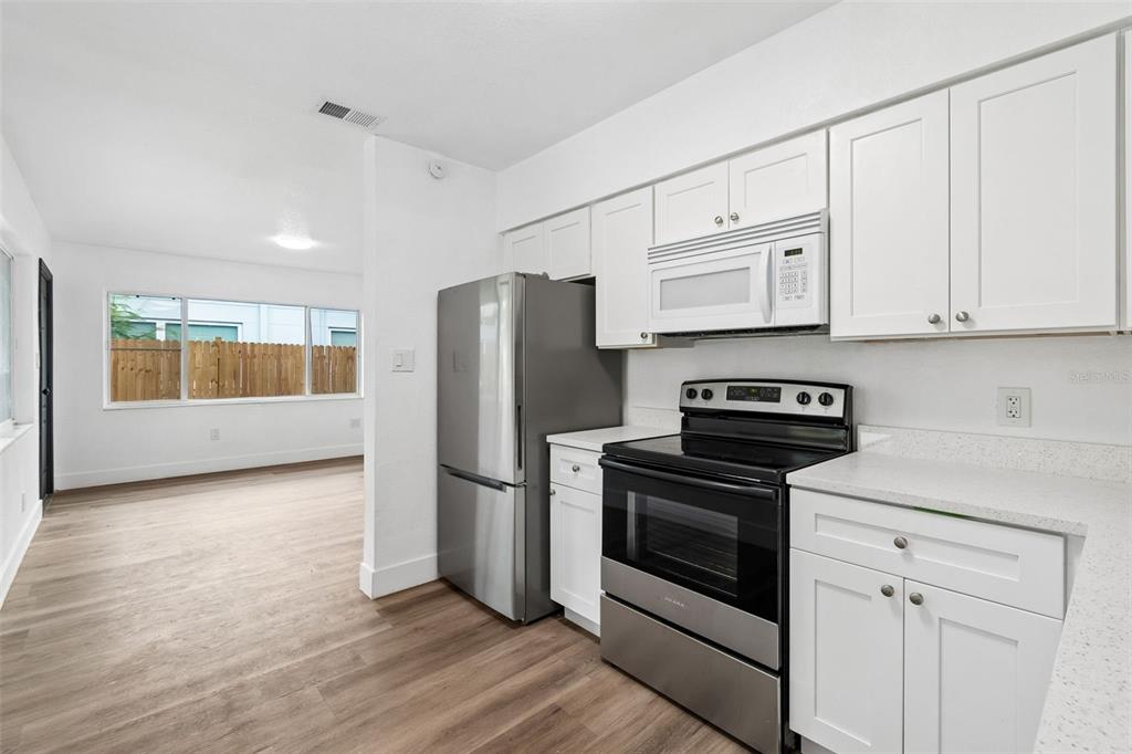 A kitchen with white cabinets and stainless steel appliances opens into a living area — 2832 MIRIAM STREET S, ST PETERSBURG, FL