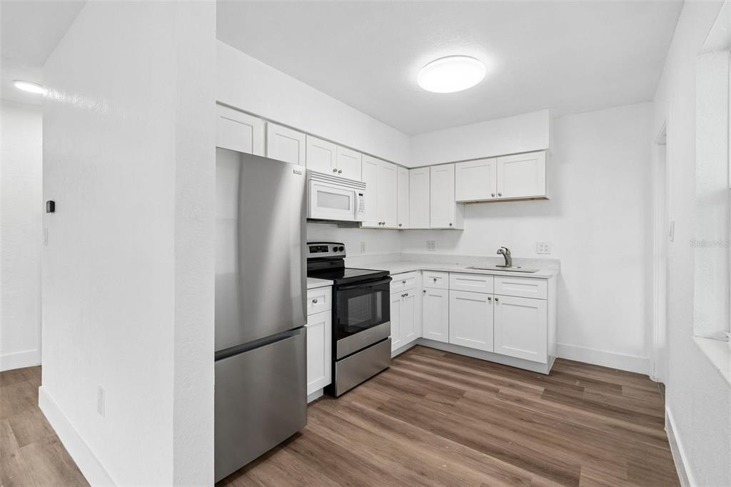 A kitchen features white cabinets, stainless steel appliances, and wood-look flooring — 2832 MIRIAM STREET S, ST PETERSBURG, FL