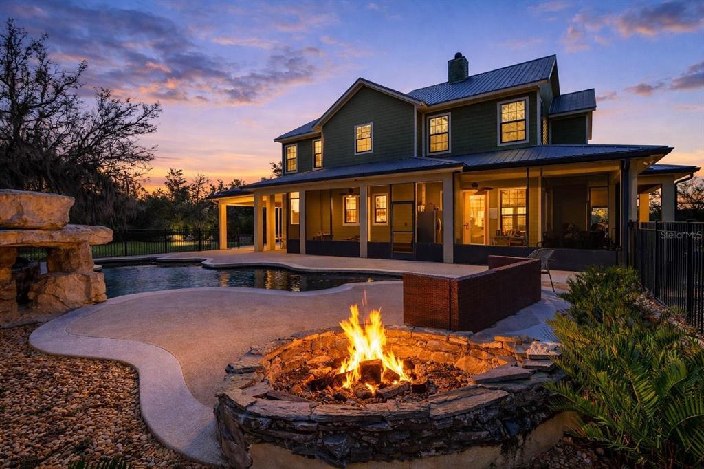 A two-story green house with a pool, stone fire pit, and patio at sunset — 326 ENTERPRISE OSTEEN ROAD, OSTEEN, FL