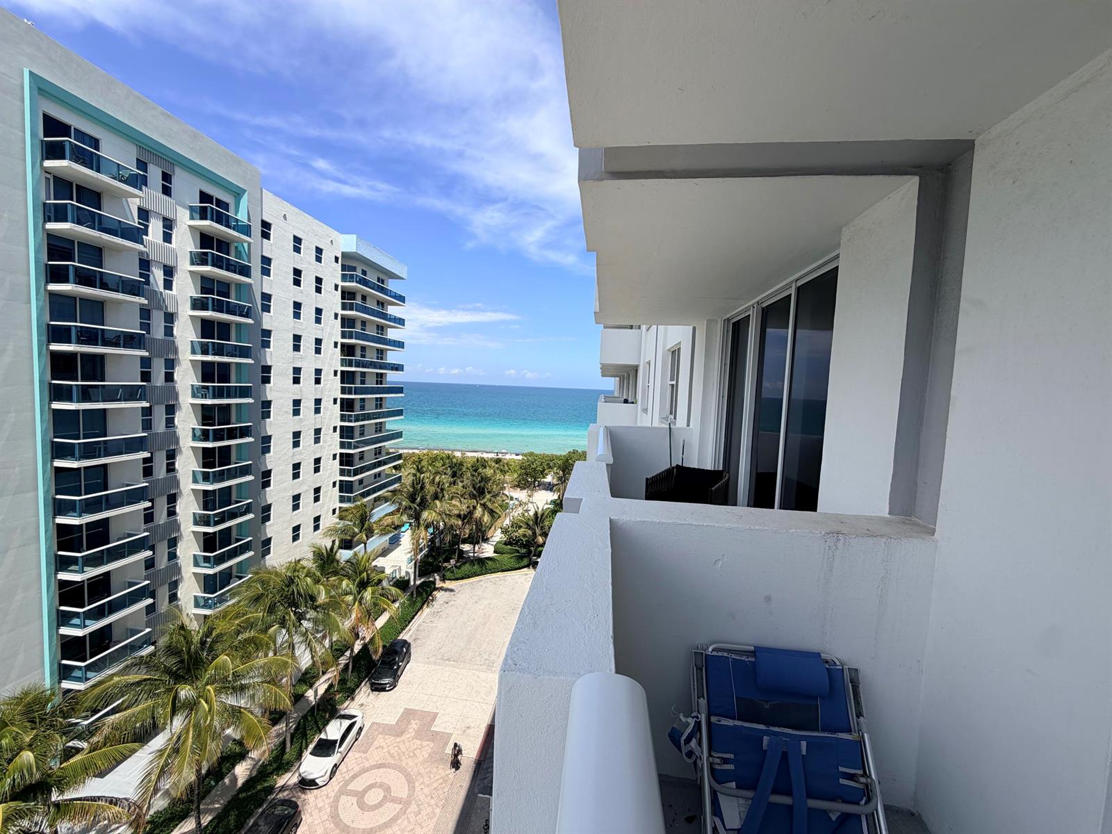 A balcony view overlooks a street, palm trees, and the ocean between two high-rise buildings — 9195 Collins Avenue # 913, Surfside FL 33154, SURFSIDE, FL