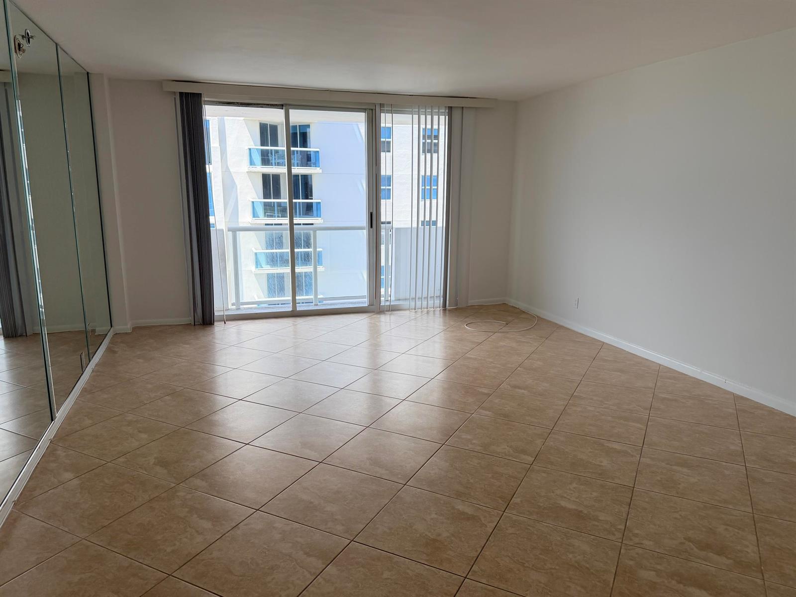 An empty room with beige tile flooring, mirrored closet doors, and a sliding glass door — 9195 Collins Avenue # 913, Surfside FL 33154, SURFSIDE, FL