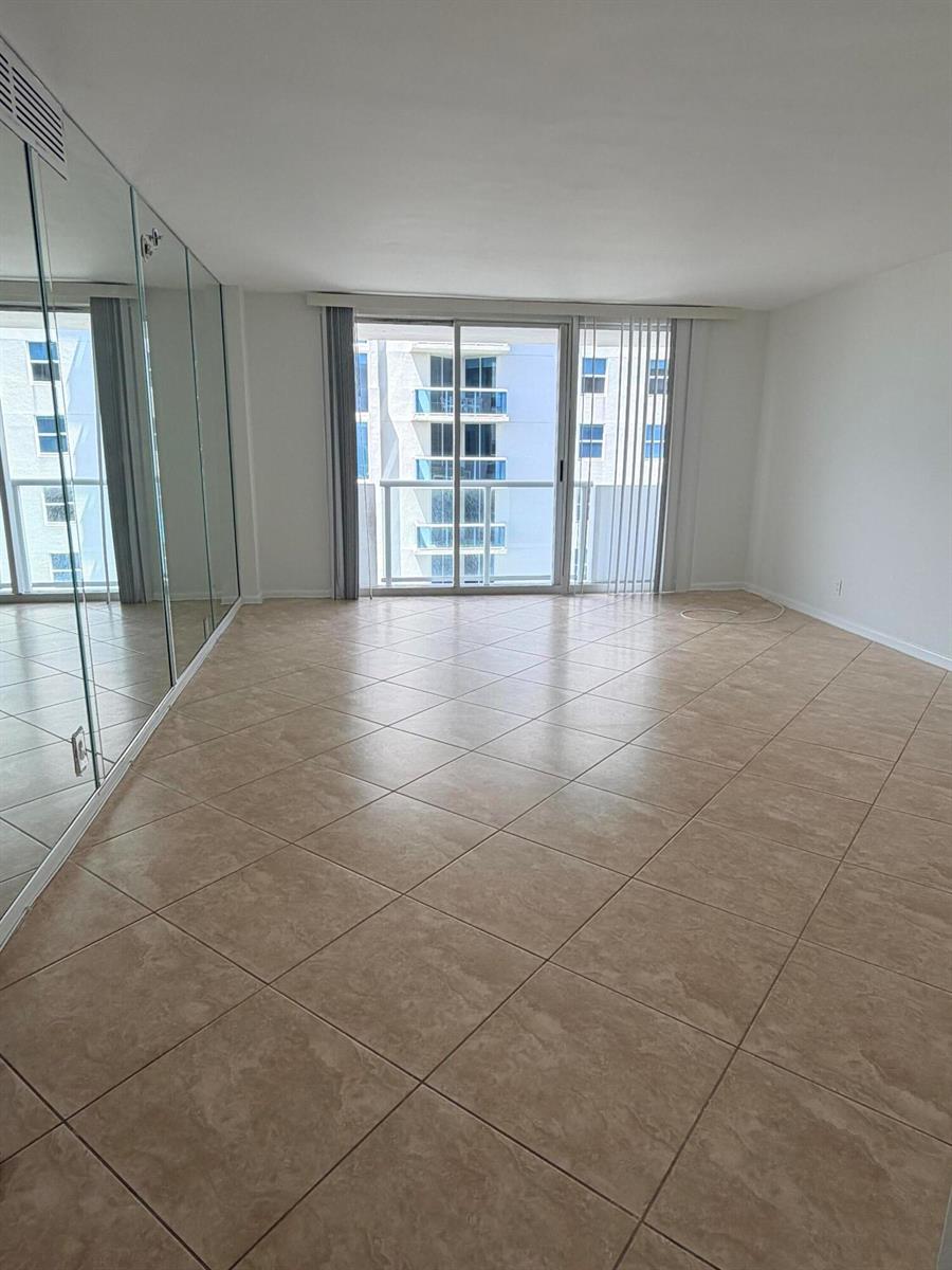 An empty room features beige tile flooring, mirrored closet doors, and a sliding glass balcony door — 9195 Collins Avenue # 913, Surfside FL 33154, SURFSIDE, FL