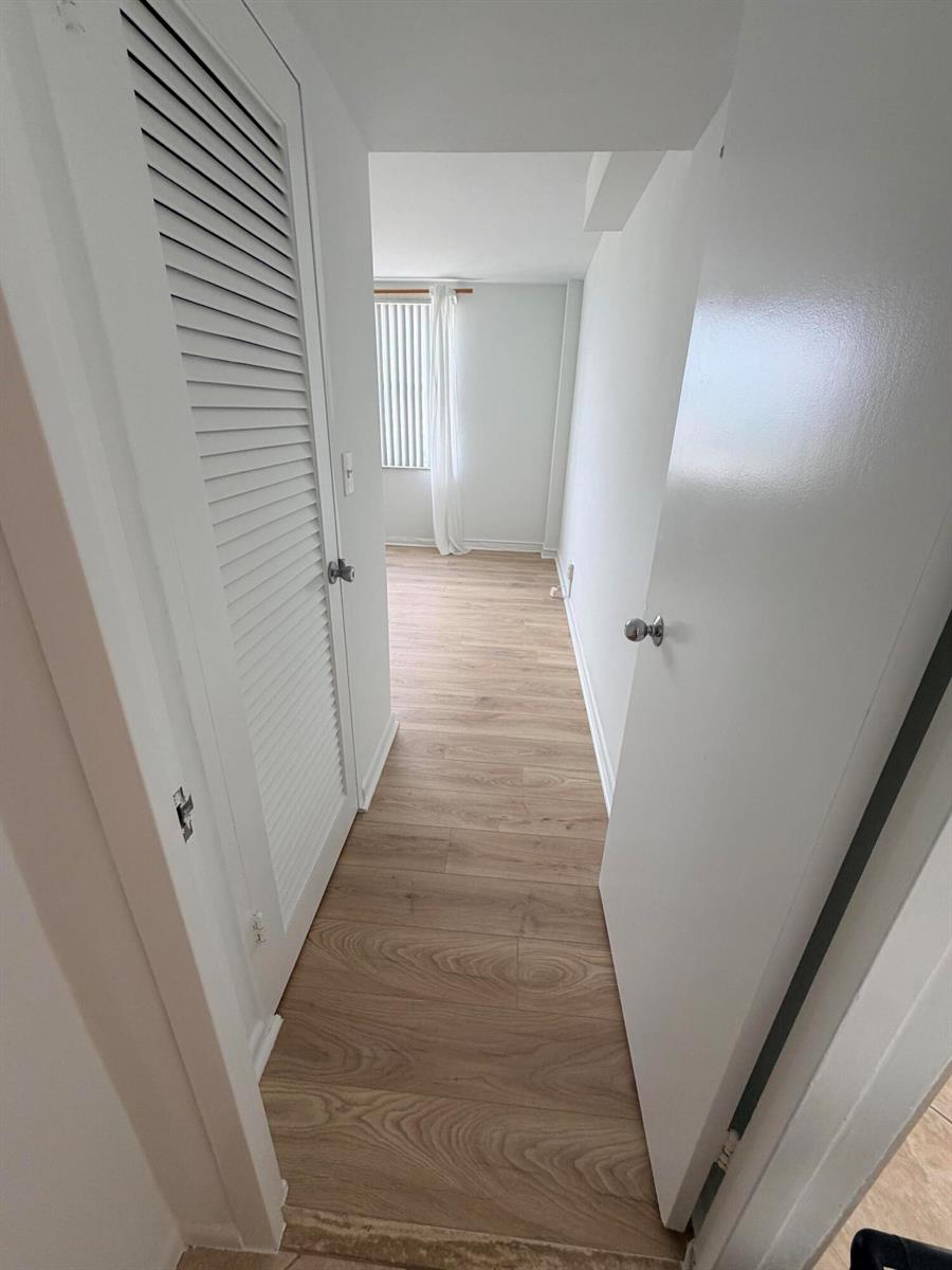 A narrow hallway with light wood-look flooring leads to a room with a window — 9195 Collins Avenue # 913, Surfside FL 33154, SURFSIDE, FL