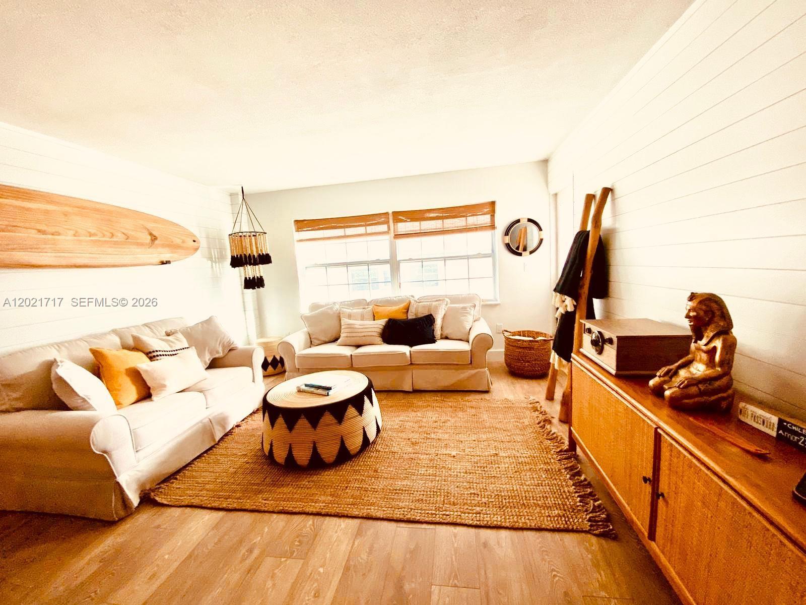 A living room features two beige sofas, a round patterned ottoman, and wood-paneled walls — 325 Ocean Dr # 408, Miami Beach FL 33139, MIAMI BEACH, FL