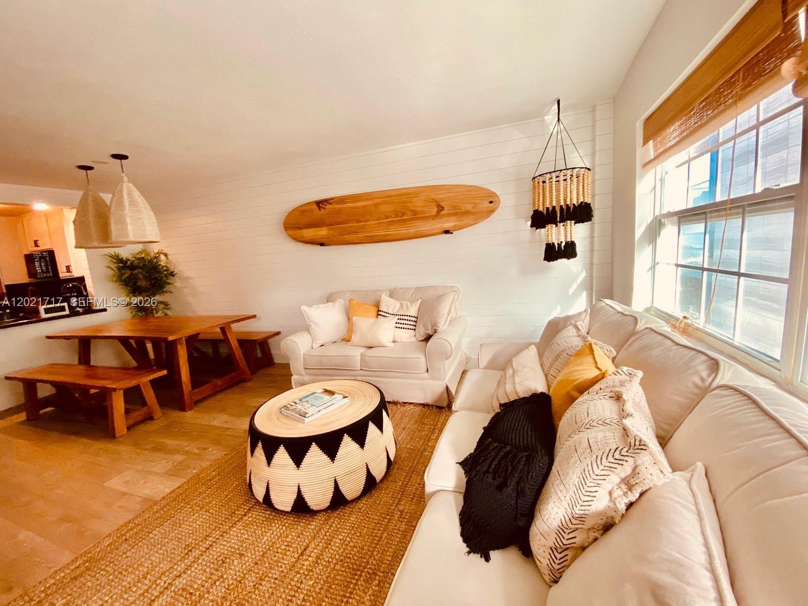 A living room features a surfboard wall decoration, a round patterned ottoman, and white sofas — 325 Ocean Dr # 408, Miami Beach FL 33139, MIAMI BEACH, FL