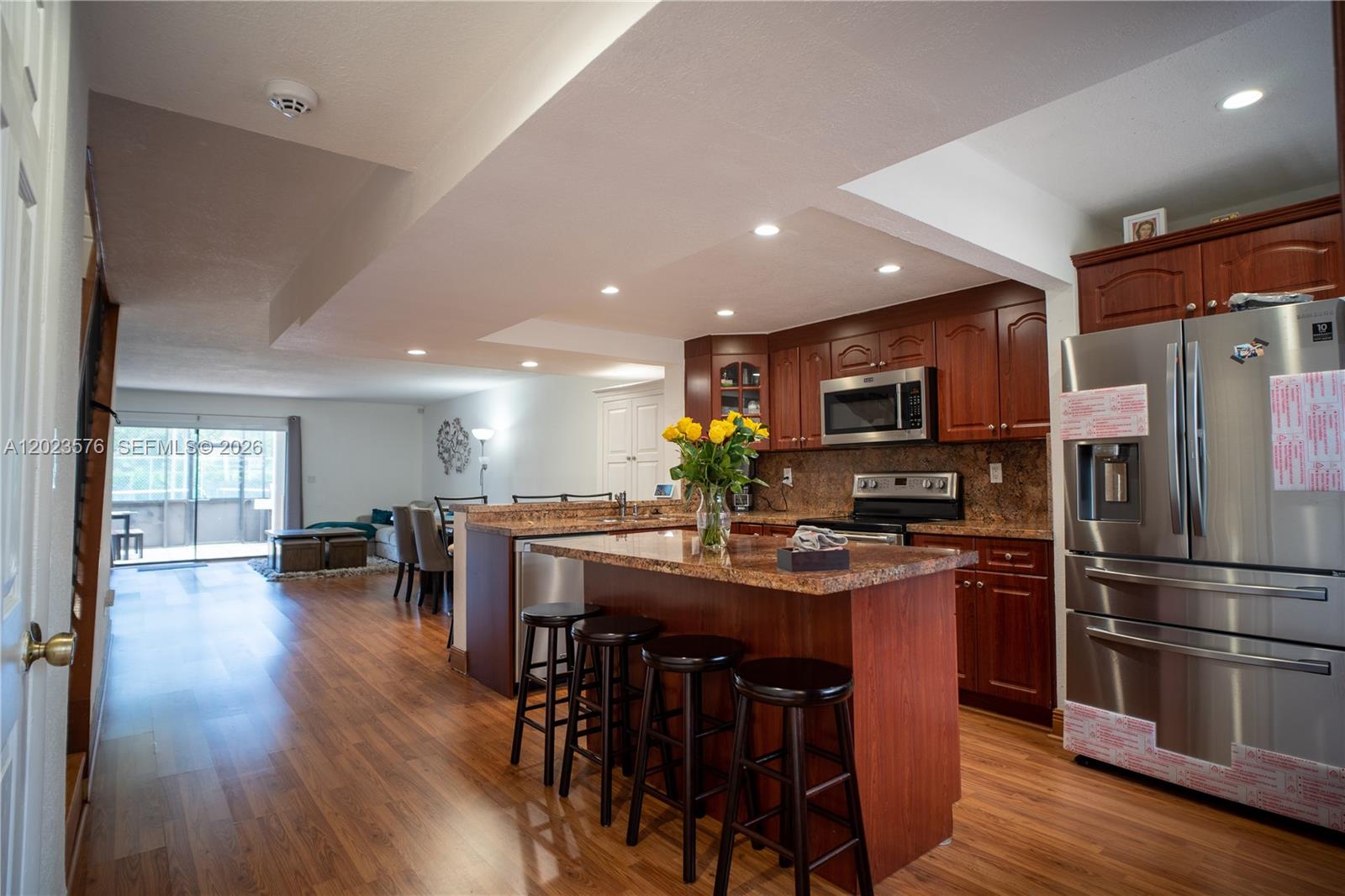 A kitchen with wood cabinets and a granite island features bar stools and wood flooring — 10052 NW 41st St # 5, Doral FL 33178, DORAL, FL
