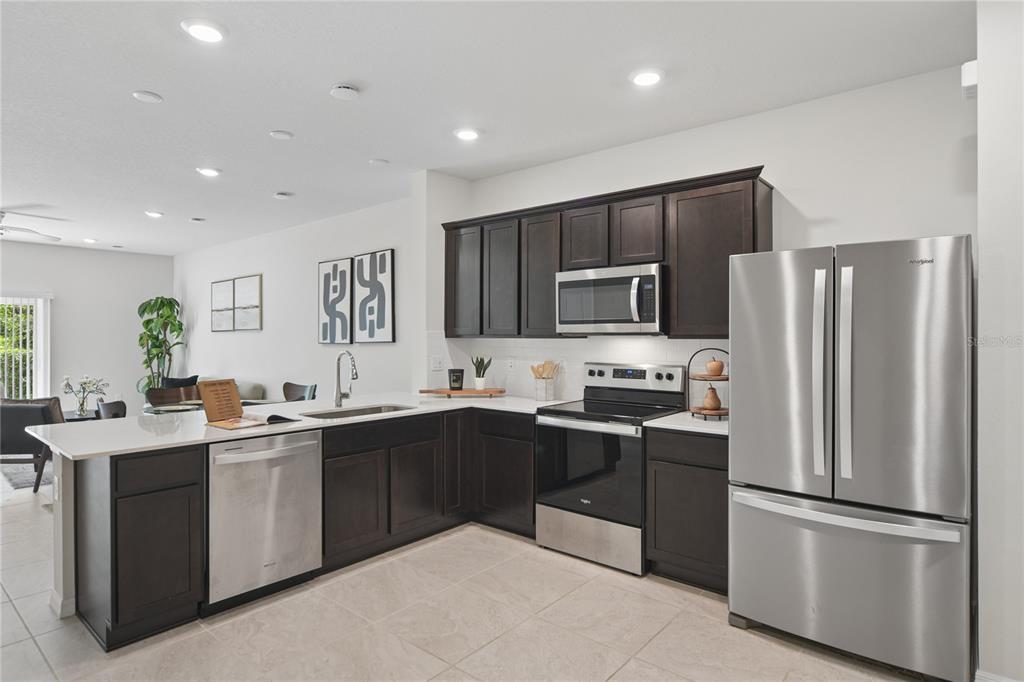 A kitchen features dark wood cabinets, stainless steel appliances, and a white quartz countertop island — 4705 SPARKLING SHELL AVENUE, KISSIMMEE, FL
