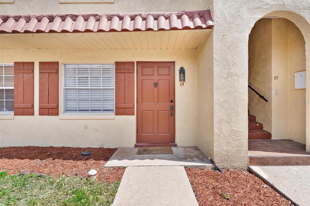 The exterior of a tan stucco townhouse features a brown front door and arched entryway — 1112 W MAIN STREET UNIT C4, LEESBURG, FL