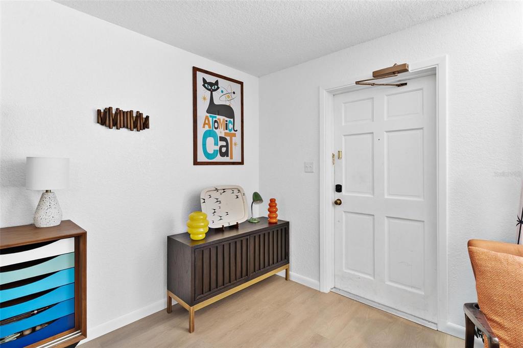 An entryway features a dark wood console table, a framed Atomic Cat poster, and light flooring — 1112 W MAIN STREET UNIT C4, LEESBURG, FL