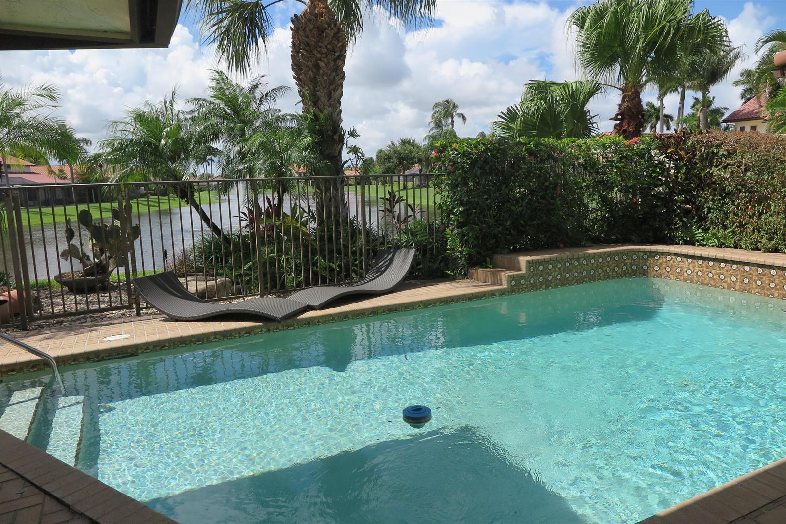 A swimming pool with lounge chairs sits on a patio overlooking a lake and palm trees — 22519 W Esplanada Cir W, Boca Raton FL 33433, BOCA RATON, FL