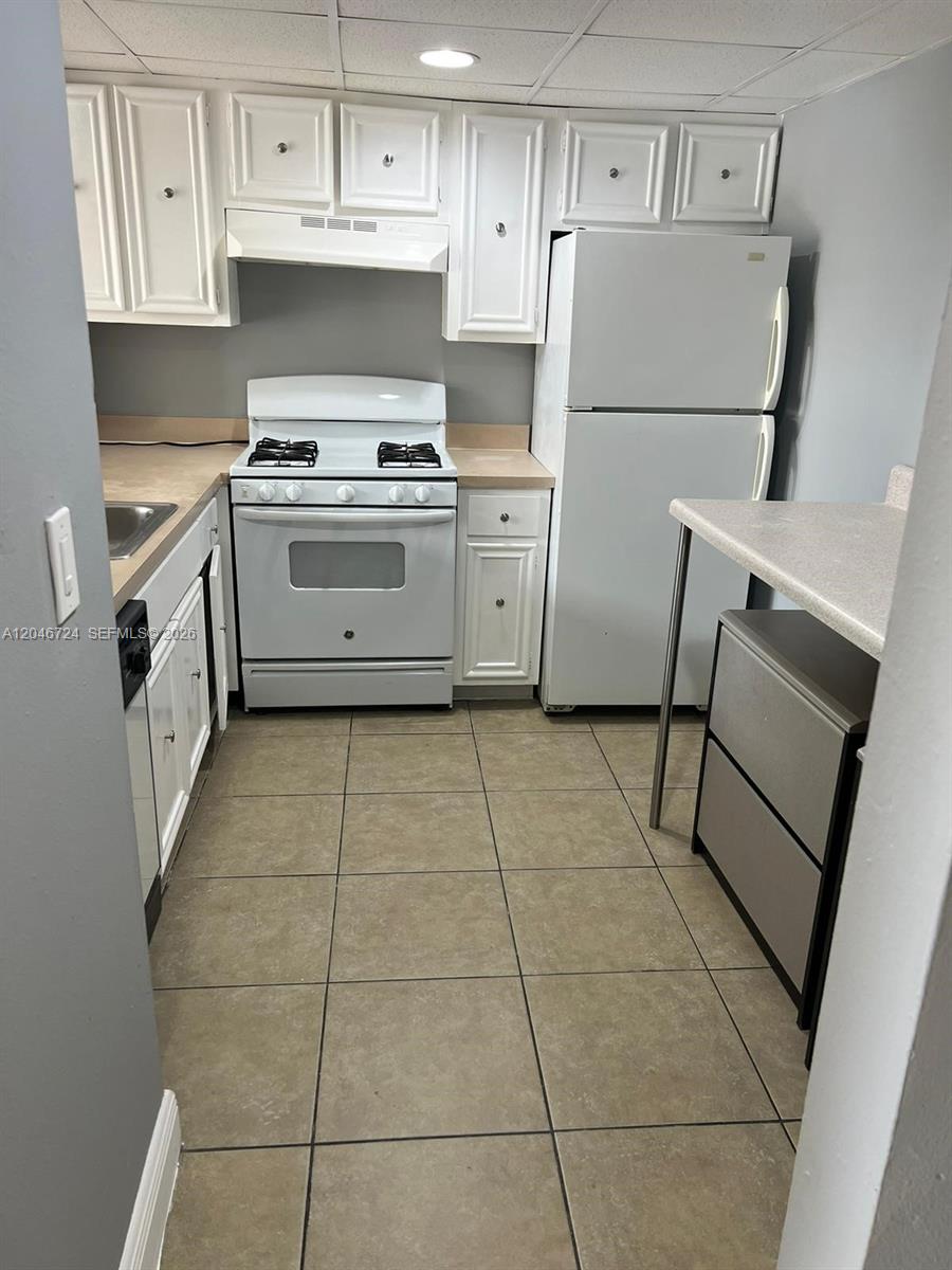 A kitchen features white cabinets, white appliances, tan countertops, and light-colored tile flooring — 18051 NW 68th Ave # 204, Hialeah FL 33015, HIALEAH, FL