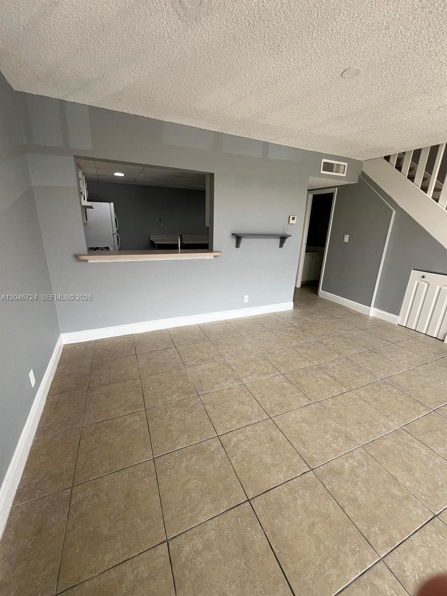 This living room features gray walls, tan tile flooring, and a kitchen pass-through window — 18051 NW 68th Ave # 204, Hialeah FL 33015, HIALEAH, FL